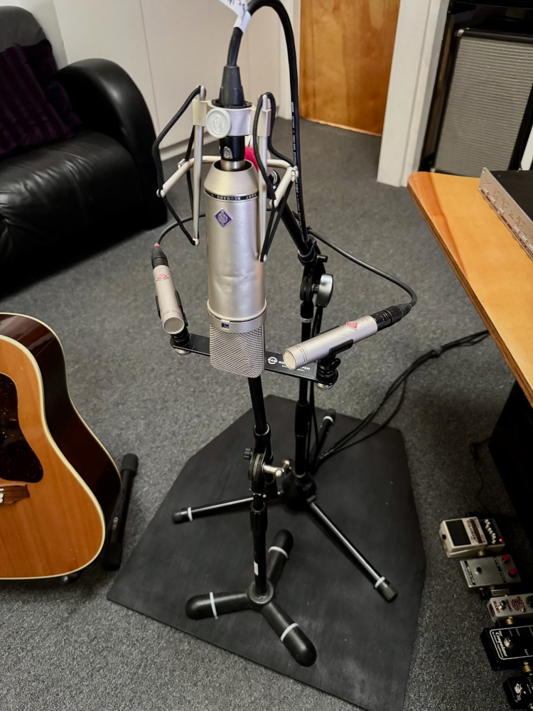 A set of microphones secured to a contraption in a recording studio, with an acoustic guitar beside it.
